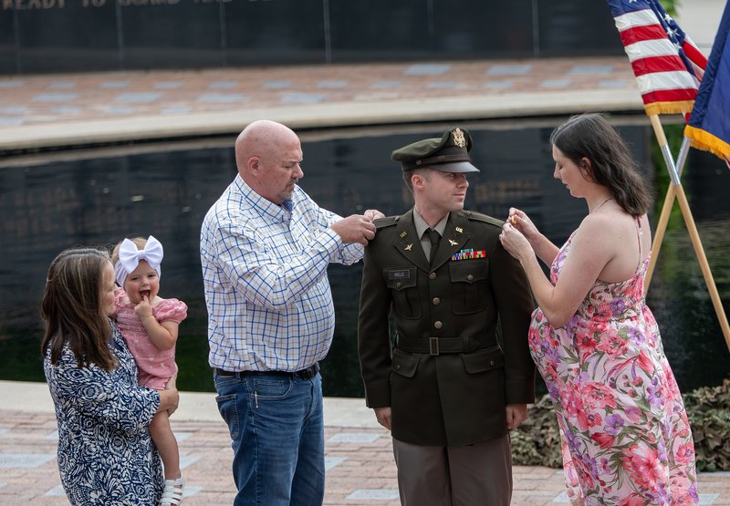 A man and a woman pin bars on the shoulders of a new Army officer.